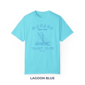 Peut inclure: Un t-shirt bleu clair avec un graphique d'un voilier et le texte "MONACO Monte Carlo YACHT CLUB Est 1953".