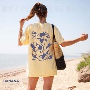 May include: A yellow t-shirt with a graphic of orcas and the text "Love, Protect & Respect Our Intellect". The person wearing the shirt is standing on a beach.