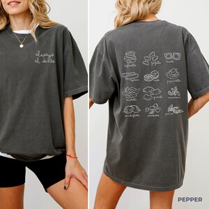 May include: A dark gray t-shirt with the text "always al dente" on the front and illustrations of different types of pasta on the back. The shirt is made of a soft, comfortable material and has a relaxed fit.