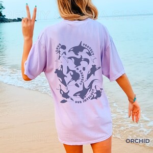 May include: A lavender t-shirt with a graphic of orcas and the text "Love, Protect & Respect Our Intellect" printed on the back.
