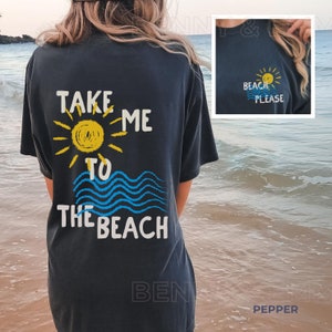 May include: A black t-shirt with the text "Take me to the beach" printed on the back. The text is in white and yellow with a blue and yellow sun and waves graphic. The front of the shirt has a small yellow sun with the text "Beach Please" in white.