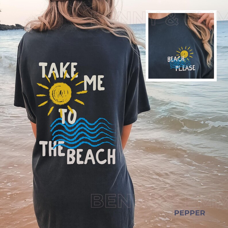 May include: A black t-shirt with the text "Take me to the beach" printed on the back. The text is in white and yellow with a blue and yellow sun and waves graphic. The front of the shirt has a small yellow sun with the text "Beach Please" in white.