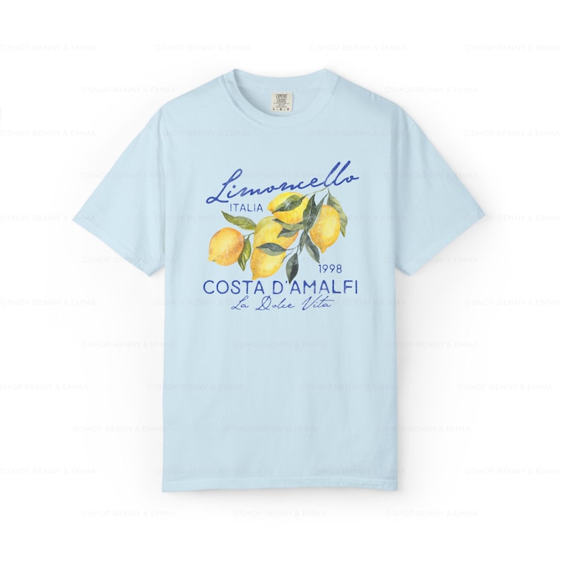 Puede incluir: Camiseta azul claro con un gr&aacute;fico de limones en una rama, el texto "Limoncello Italia 1998 Costa D'Amalfi La Dolce Vita" est&aacute; impreso en la camiseta.