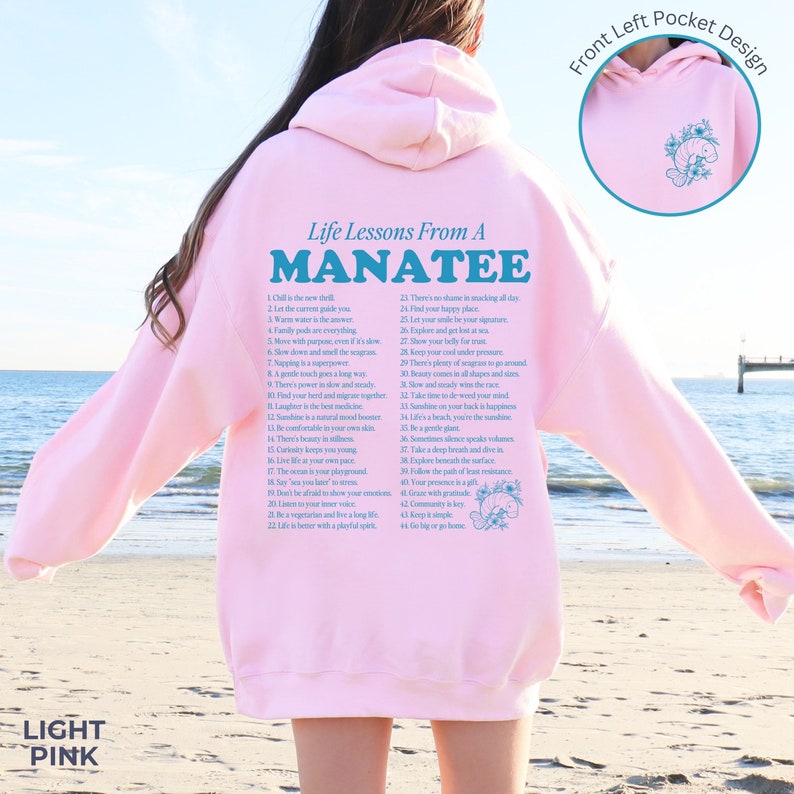 K&ouml;nnte beinhalten: Ein hellrosa Hoodie mit einem blauen Grafikdruck eines Manati und dem Text "Life Lessons From A Manatee" mit einer Liste von 43 Lebenslektionen. Der Hoodie hat eine Fronttasche mit einem kleinen Grafikdruck eines Manati.