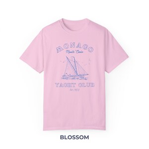 Peut inclure: Un t-shirt rose avec un graphique bleu d'un voilier et le texte "MONACO Monte Carlo YACHT CLUB Est/1953".
