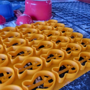 May include: A close-up of a baking sheet filled with yellow plastic fish-shaped cookie cutters. The cutters are arranged in rows and are ready to be used for baking.