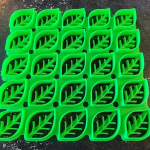 Peut inclure: Un moule en silicone vert vif avec 25 cavités en forme de feuille. Le moule est conçu pour la cuisson et la création d'articles alimentaires décoratifs.