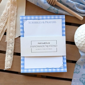 May include: A white ceramic mug with a black handle and the text "But First, Coffee" in a black, bold font. The mug is on a white surface.