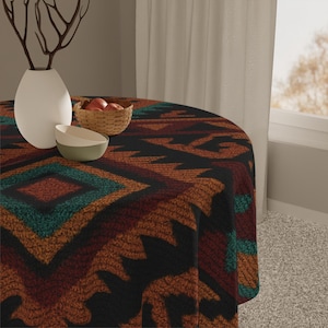 May include: A round tablecloth with a geometric pattern in shades of black, brown, orange, and teal. The tablecloth is on a round table. A white vase, a small bowl, and a basket of apples are on the table.