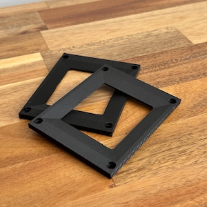 May include: Two black plastic frames with rounded corners and small holes on the edges. The frames are stacked on top of each other.