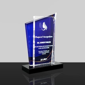 May include: A clear and blue acrylic plaque with the text "Plaque of Recognition" and "DR. ANDREW POBLETE". The plaque is mounted on a black base and features a logo and inscription.