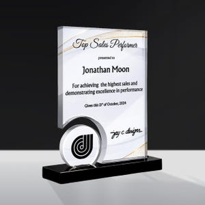 Peut inclure: Une plaque de récompense rectangulaire en acrylique transparent sur un socle noir. Le texte indique Top Sales Performer, presented to Jonathan Moon, For achieving the highest sales and demonstrating excellence in performance, Given this 21st of October, 2024, jay c. designs.