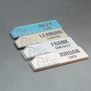 May include: Four rectangular name badges with a pointed left edge, arranged in a stack. Each badge features the text Allen Real Estate in script, followed by a person's name in block letters: Riley Stone, Leandro Carrera, Frank Gonzalez, and Jordan Chen.