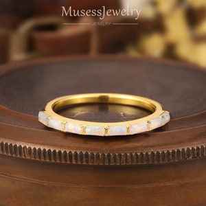 May include: A gold band ring with a row of white opal stones. The ring is on a brown surface.