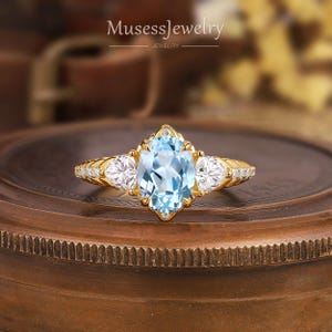 May include: A gold ring with a large oval-shaped blue topaz gemstone surrounded by smaller diamonds. The ring has a delicate, intricate design.