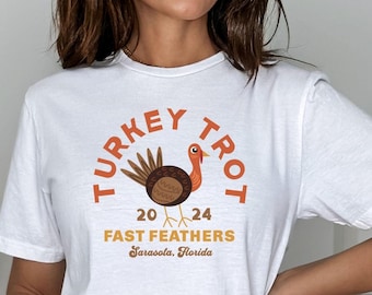 May include: White t-shirt with a brown and orange turkey graphic. The text "TURKEY TROT 20 24 FAST FEATHERS Sarasota, Florida" is printed on the shirt.