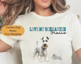 May include: White t-shirt featuring a graphic of a white miniature schnauzer dog and the text "LOVE MY SCHNAUZER Gracie". The shirt is being worn by a woman in blue jeans. The text "Custom Dog Name Free Shipping" is in a circle on the left side of the shirt.
