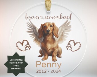 May include: A round, clear glass ornament with a brown dachshund with angel wings. The ornament has the text "forever remembered" at the top and "Penny 2012-2024" at the bottom. There are two hearts with paw prints on either side of the dog.