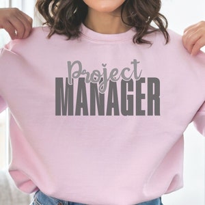 May include: A light pink sweatshirt with the text "Project Manager" in gray lettering.