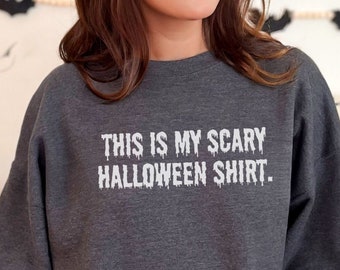 May include: Dark heather gray sweatshirt with the text "THIS IS MY SCARY HALLOWEEN SHIRT" in white. The text has a dripping effect. The sweatshirt is a crew neck style.