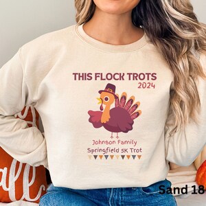May include: Sand-coloured sweatshirt featuring a turkey graphic and the text "THIS FLOCK TROTS 2024". The turkey wears a hat and has a maroon body and tail feathers. Below the turkey is the text "Johnson Family Springfield 5K Trot".