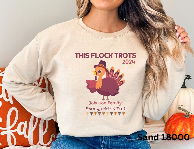 May include: Sand-coloured sweatshirt featuring a turkey graphic and the text "THIS FLOCK TROTS 2024". The turkey wears a hat and has a maroon body and tail feathers. Below the turkey is the text "Johnson Family Springfield 5K Trot".