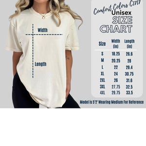 Op de afbeelding: Cr&egrave;mekleurig unisex T-shirt met een maattabel. De tabel toont maten S tot 4XL, met breedte- en lengtematen in inches. Het model is 1,57 m lang en draagt maat M. Het shirt is van Comfort Colors C1717.