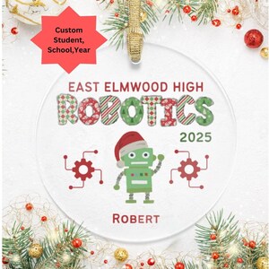 May include: Clear, round Christmas ornament with the text "EAST ELMWOOD HIGH ROBOTICS 2025" and a green robot wearing a Santa hat. The name "ROBERT" is below the robot. Red and green accents and a gold hanging loop.
