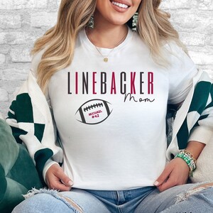Puede incluir: Camiseta blanca con el texto "Linebacker Mom" y un gr&aacute;fico de f&uacute;tbol con el nombre "Michael #42".