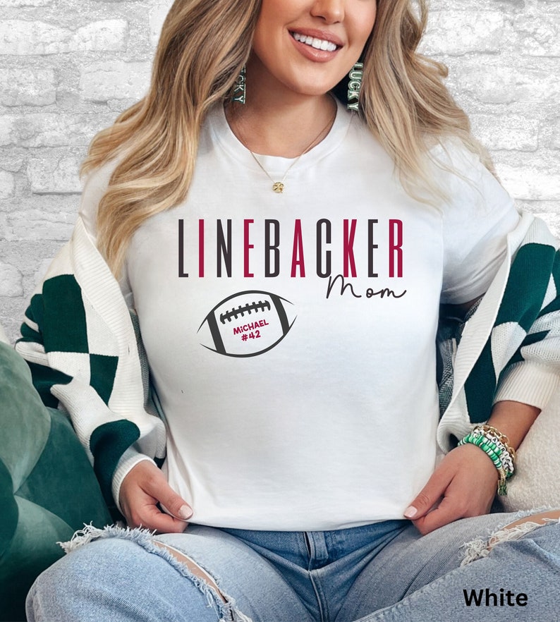 Puede incluir: Camiseta blanca con el texto "Linebacker Mom" y un gr&aacute;fico de f&uacute;tbol con el nombre "Michael #42".