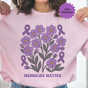May include: Pink sweatshirt with a purple flower design and the text "Memories Matter". The flowers are surrounded by purple ribbons.
