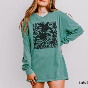 Op de afbeelding: Lichtgroen shirt met lange mouwen met een zwarte afbeelding van orka's, vissen en een octopus. Het shirt heeft een relaxte pasvorm en een ronde hals. De tekst "Light Green" is rechtsonder zichtbaar.