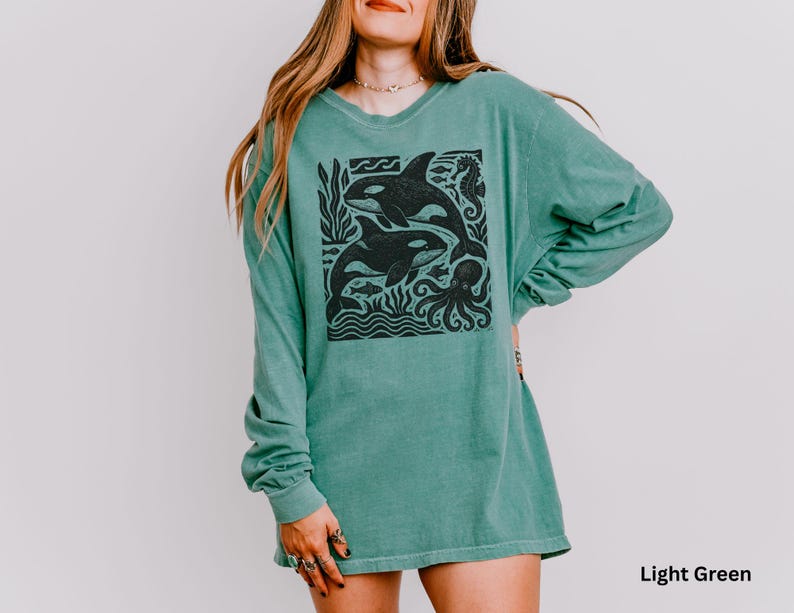 Op de afbeelding: Lichtgroen shirt met lange mouwen met een zwarte afbeelding van orka's, vissen en een octopus. Het shirt heeft een relaxte pasvorm en een ronde hals. De tekst "Light Green" is rechtsonder zichtbaar.