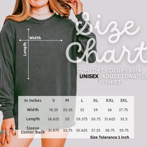 Op de afbeelding: Een donkergrijs unisex T-shirt met lange mouwen en een maattabel. De tabel geeft de afmetingen in cm voor breedte, lengte en mouwcentrum achter voor de maten S t/m 3XL. Het shirt is Comfort Colors 6014.