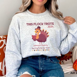 May include: Light grey sweatshirt featuring the text "THIS FLOCK TROTS 2024" and a cartoon turkey wearing a hat. The sweatshirt also includes the text "Johnson Family Springfield 5K Trot".