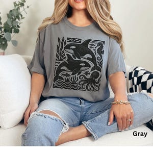 Op de afbeelding: Grijze t-shirt met een zwart-witte afbeelding van orka's, zeewier, vissen en een octopus. De t-shirt heeft korte mouwen en een ronde hals. Het woord "Gray" staat rechtsonder afgedrukt.