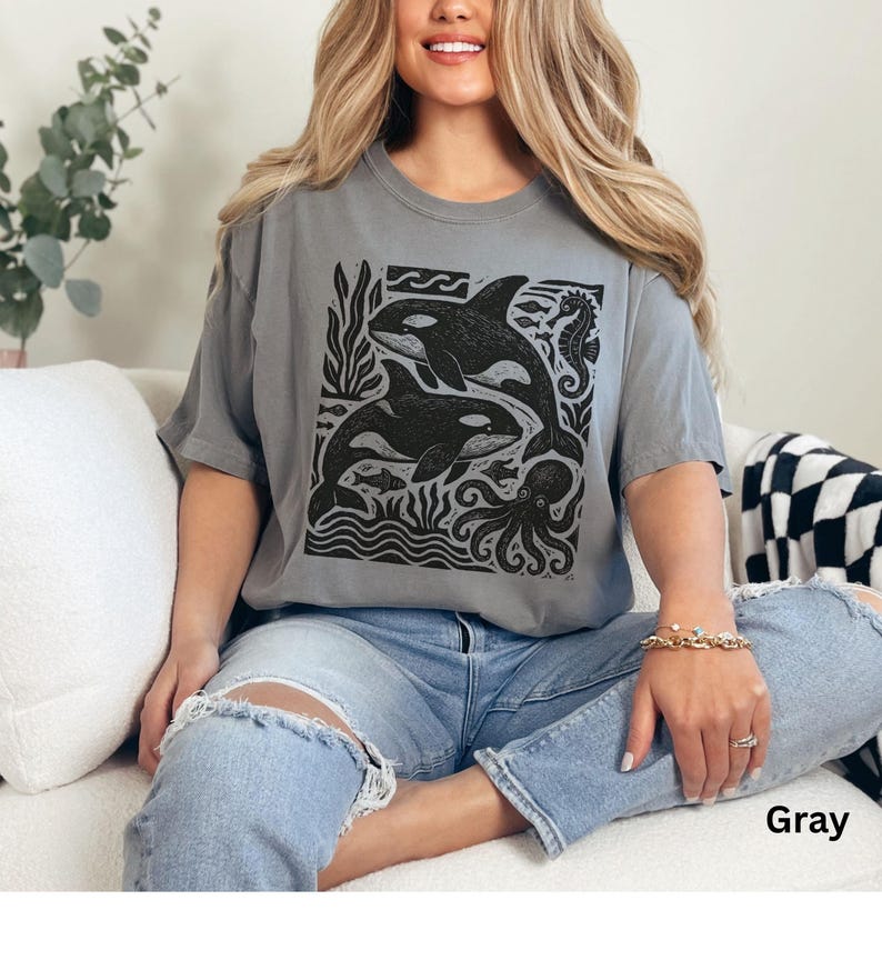 Op de afbeelding: Grijze t-shirt met een zwart-witte afbeelding van orka's, zeewier, vissen en een octopus. De t-shirt heeft korte mouwen en een ronde hals. Het woord "Gray" staat rechtsonder afgedrukt.
