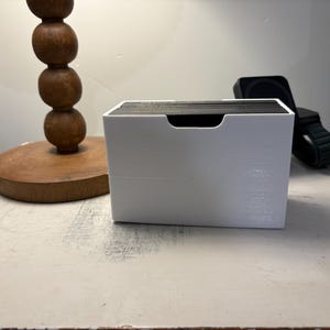 May include: White plastic card holder with a black card stack inside. The holder is sitting on a white surface.