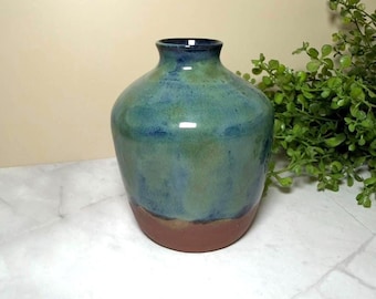 Pode incluir: Um vaso de cerâmica com corpo arredondado e pescoço estreito. A parte superior apresenta um esmalte brilhante em tons misturados de azul e verde, enquanto a base inferior permanece sem esmalte em uma cor marrom terracota fosca.