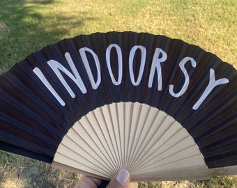 Op de afbeelding: Een zwarte vouwwaaier met een witte inscriptie die "Indoorsy" zegt.