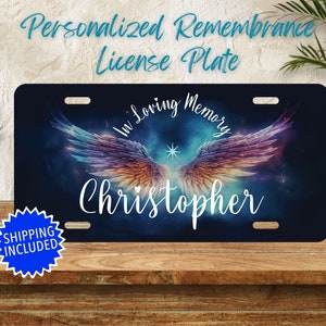 May include: Personalized remembrance license plate with a blue, purple, and orange angel wing design. The text "In Loving Memory" is above the wings and the name "Christopher" is below the wings.