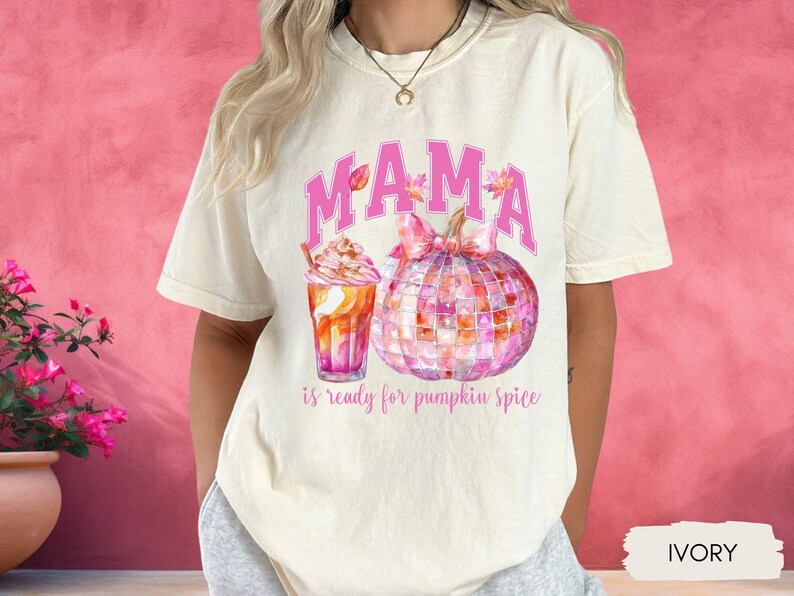 May include: A white t-shirt with the text "MAMA is ready for pumpkin spice" in pink lettering. The shirt features a watercolor illustration of a pumpkin and a cup of coffee.