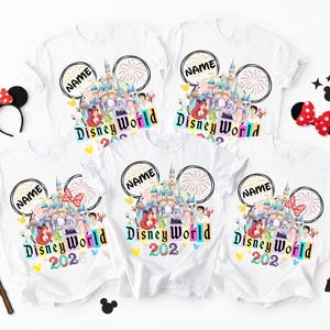 Puede incluir: Camisetas blancas con un dise&ntilde;o colorido de Disney World con un castillo, personajes y el texto "Disney World 2026". Las camisetas tienen un dise&ntilde;o de orejas de Mickey Mouse con la palabra "NAME" y fuegos artificiales. Accesorios: orejas de Minnie y una varita de guante de Mickey.