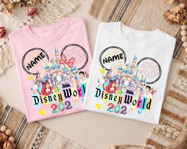 Puede incluir: Dos camisetas, una rosa y otra blanca, con un dise&ntilde;o de Disney World. El dise&ntilde;o incluye un castillo, personajes y las palabras "Disney World 2023". Cada camiseta tiene un contorno de oreja de Mickey Mouse negro y la palabra "NAME".