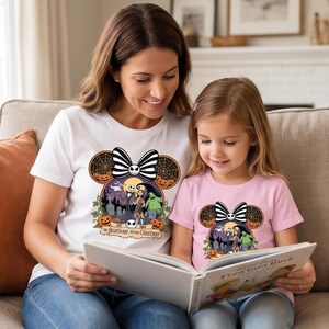 Op de afbeelding: Wit T-shirt met een zwart-witte strik en een Halloween-thema grafisch ontwerp. De afbeelding bevat personages uit "The Nightmare Before Christmas" en de tekst "The Nightmare Before Christmas". Een roze T-shirt met een vergelijkbaar ontwerp is ook zichtbaar.