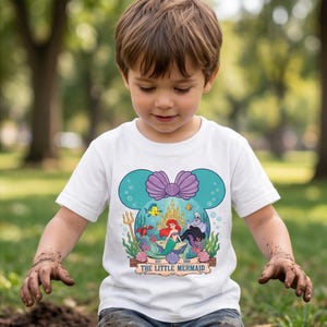 Puede incluir: Camiseta blanca con un gr&aacute;fico colorido de La Sirenita de Disney. El dise&ntilde;o incluye a Ariel, Flounder, Sebasti&aacute;n y &Uacute;rsula, dentro de un marco con forma de Mickey Mouse. La camiseta tiene el texto "The Little Mermaid" y "Est. 1989".