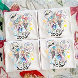 May include: Four white t-shirts with a Disney-themed graphic featuring characters, a castle, and the text "Disney 2026". Each shirt has a space for a name. Decorative bows and a fairy wand are visible.