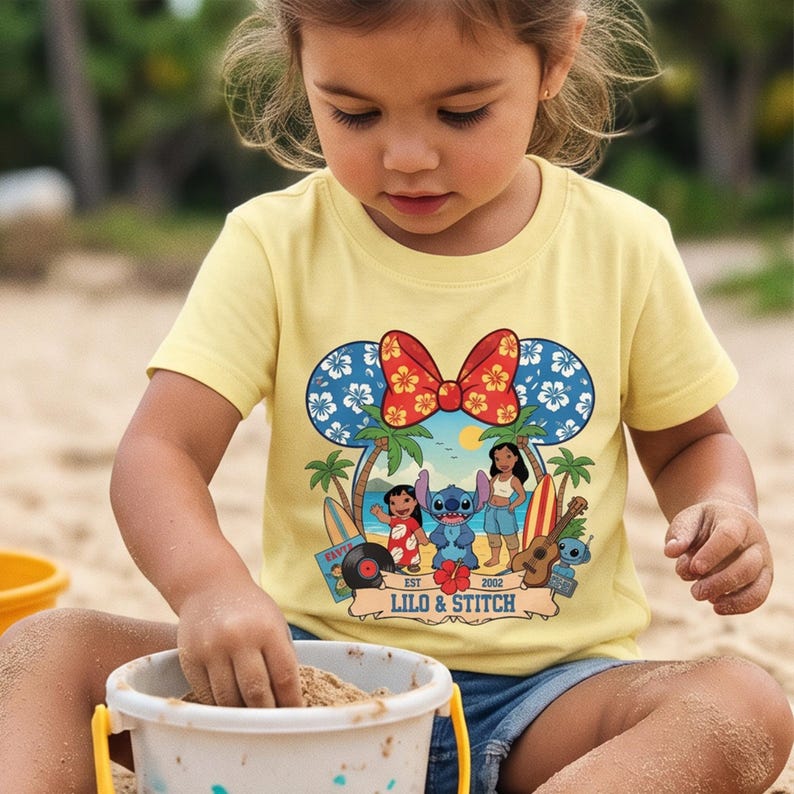 May include: A yellow t-shirt featuring a graphic of Lilo & Stitch. The design includes a Mickey Mouse-shaped head with blue floral ears and a red bow. The shirt has the text "Lilo & Stitch" and the year "2002".