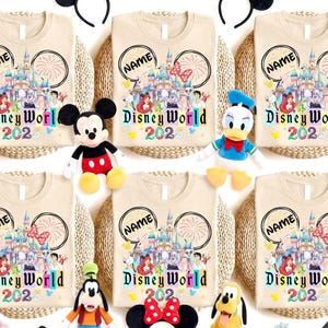 Puede incluir: Camisetas beige con un dise&ntilde;o de Disney World 2020, con un castillo, fuegos artificiales e ilustraciones de personajes. Cada camiseta tiene un espacio para un nombre dentro de las orejas de Mickey Mouse. Los personajes de peluche de Disney est&aacute;n colocados alrededor de las camisetas.