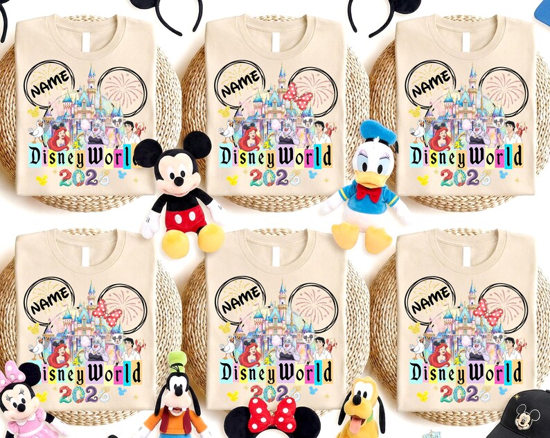 Puede incluir: Camisetas beige con un dise&ntilde;o de Disney World 2020, con un castillo, fuegos artificiales e ilustraciones de personajes. Cada camiseta tiene un espacio para un nombre dentro de las orejas de Mickey Mouse. Los personajes de peluche de Disney est&aacute;n colocados alrededor de las camisetas.